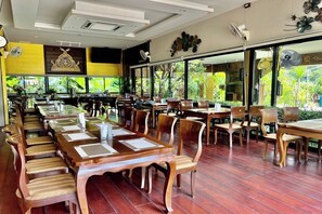 Un restaurante con largas mesas y sillas de madera, amplias ventanas con vista a zonas verdes y un diseño de techo moderno.