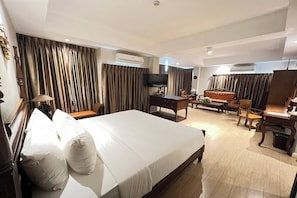 A hotel room with a large bed, a desk, a chair, a TV, and curtains.