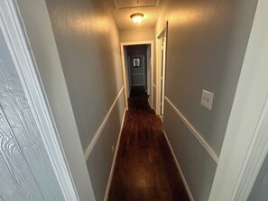 A narrow hallway with wooden flooring and light gray walls. - Charming 4br house w/ Free parking + Wifi (De Soto)