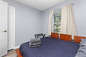 A bedroom with a bed, a chair, a door, and a window with curtains. - Charming 4br house w/ Free parking + Wifi (De Soto)