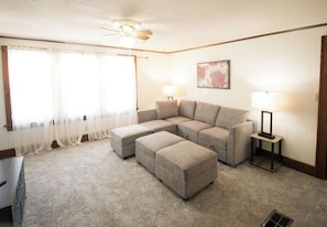 A living room with a sectional sofa, ottoman, two lamps, and a ceiling fan. - Spacious & Fun Family Home in the Heart of Emporia (Emporia)