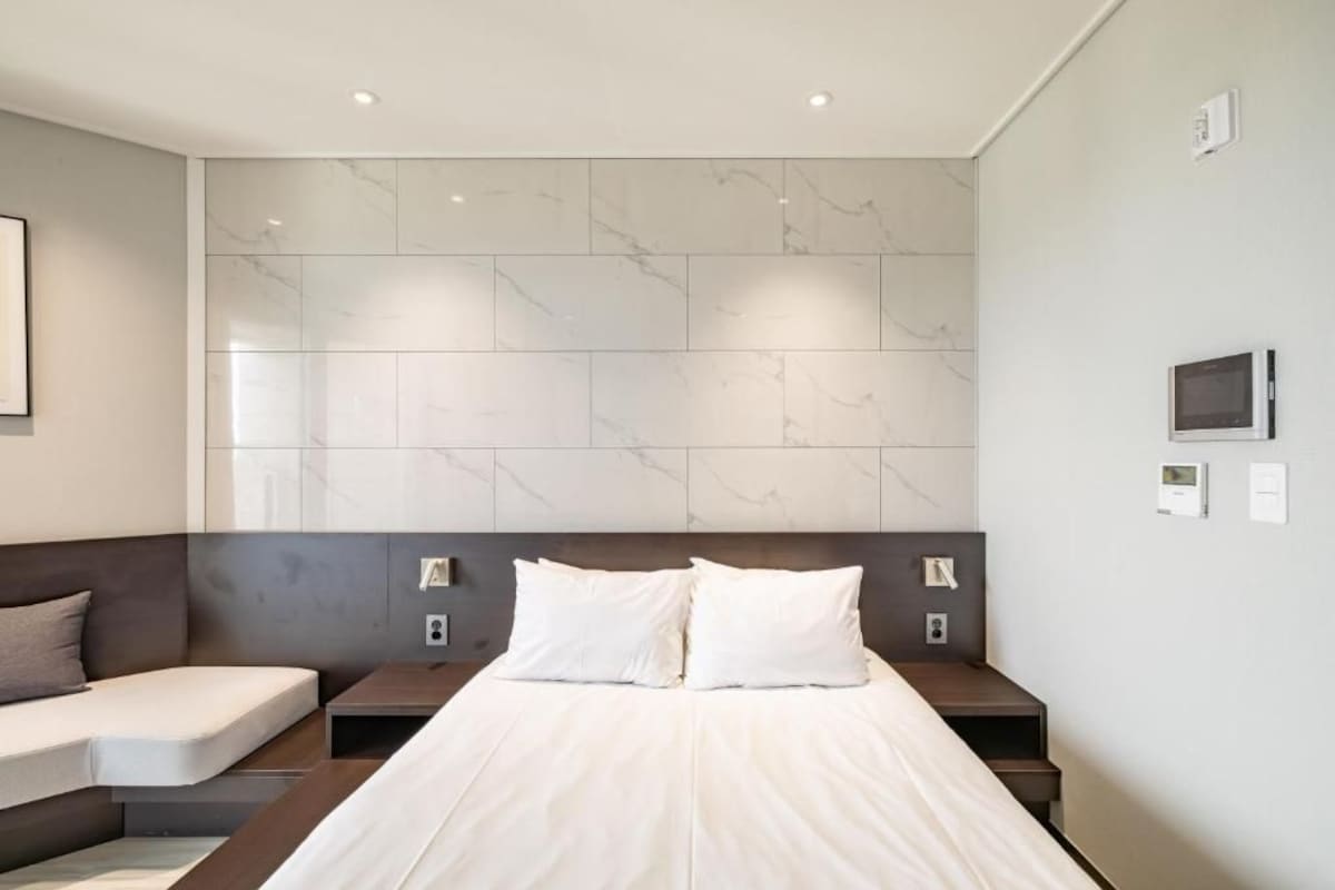 A modern hotel room with a large bed, a sofa, and a marble wall.