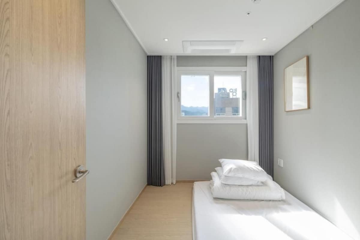A hotel room with a bed, a window, and a door.