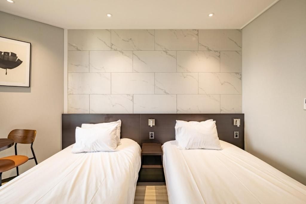 Een hotelkamer met twee enkele bedden, een nachtkastje, een stoel en een wand met een marmerlook.