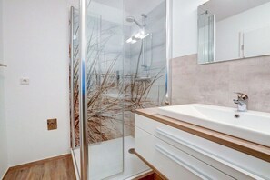 A modern bathroom with a glass shower enclosure, a white sink with a wooden countertop, and a large mirror above the sink. - Holiday apartment with 2 bedrooms (St. Peter-Ording)