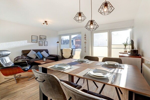 A modern living room with a dining area, leather furniture, and pendant lighting. - Holiday apartment with 2 bedrooms (St. Peter-Ording)