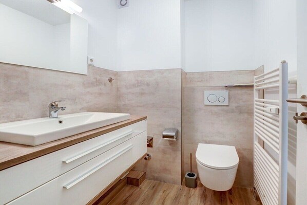 Casa de banho moderna com lavatório branco, toucador de madeira e sanita.