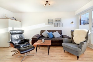 Ein modernes Wohnzimmer mit Ledersessel, Sofa, kleinem Holztisch und Lampe.