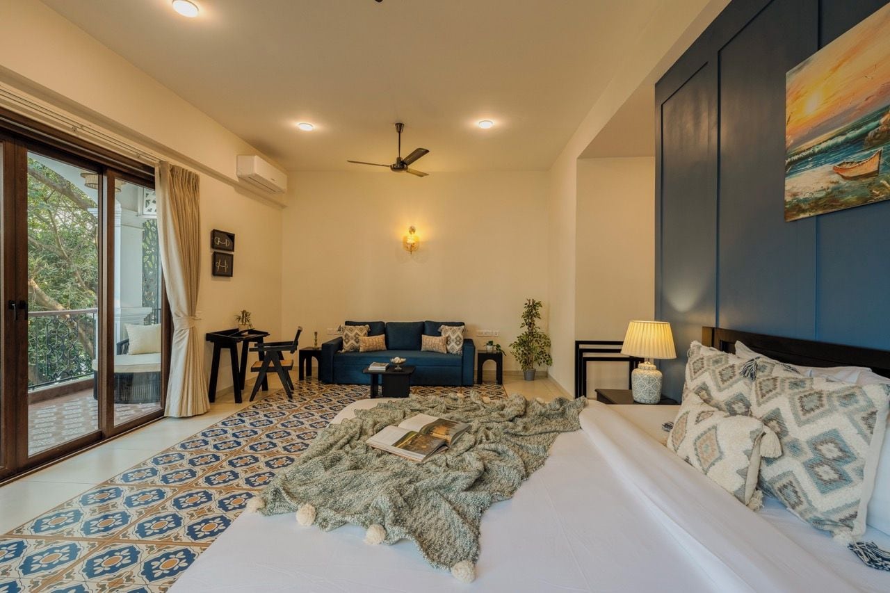 A bedroom with a bed, a sofa, a small table, a lamp, and a painting on the wall.
