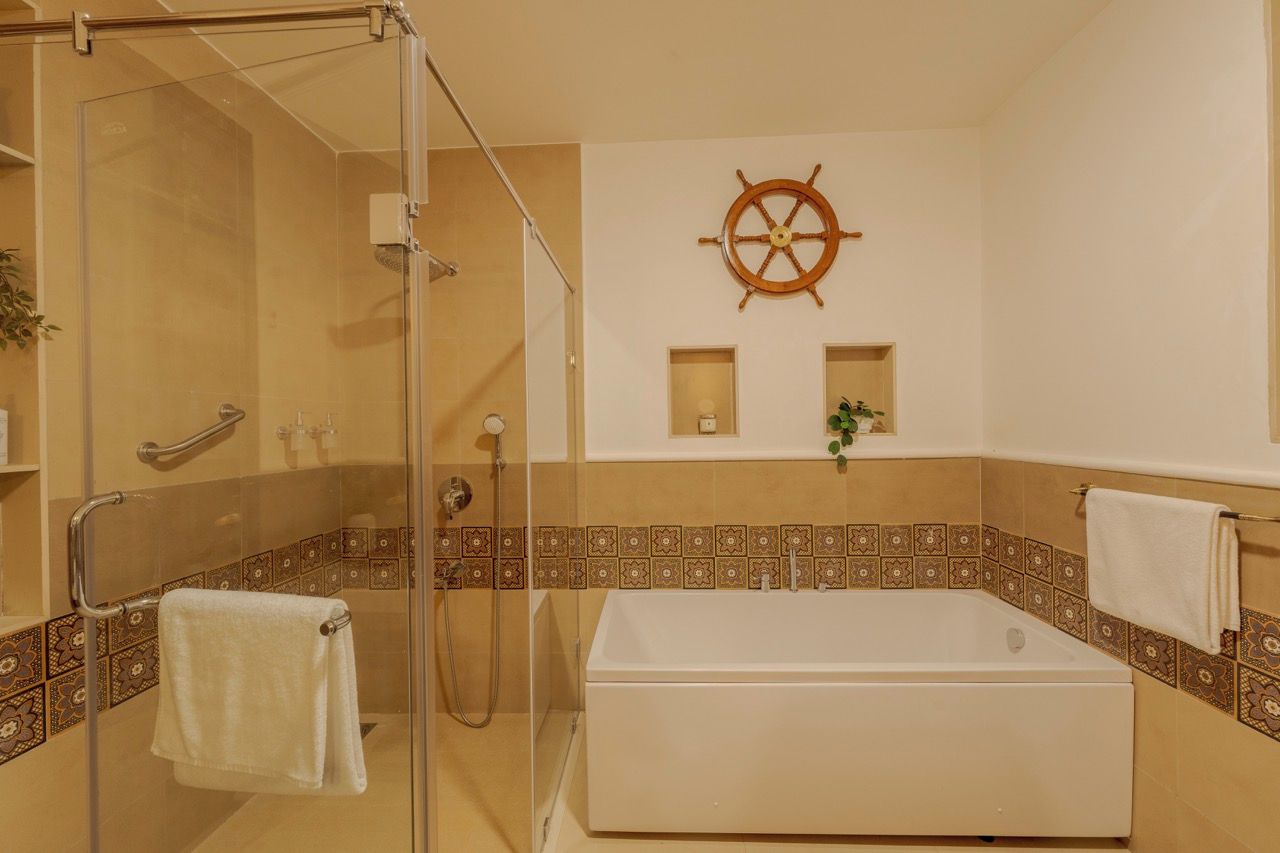 A bathroom with a glass-enclosed shower, a white bathtub, and a ship's wheel decoration on the wall.
