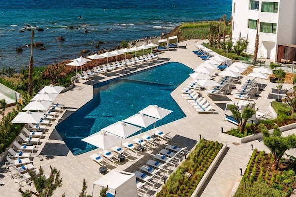 A pool area with lounge chairs and umbrellas, surrounded by greenery and a building. - Idou Malabata Beach & Spa (Tangier)