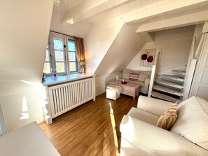 A cozy loft bedroom with a sloped ceiling, a radiator, a sofa, a coffee table, and a window with curtains. - Deichhof Holiday Apartment 8 (Dunsum)