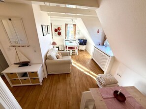 Ein gemütliches Wohnzimmer mit einer Couch, einem kleinen Tisch und einem Fernseher. Es gibt einen Essbereich mit Tisch und Stühlen. Der Raum hat Holzböden und weiße Wände.