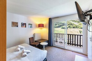 Hotelkamer met een bed, een tafel, een stoel, een lamp, een radiator en een balkon met uitzicht op de omgeving.