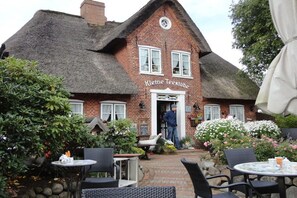 A traditional brick building with a thatched roof, named 'Kleine Teestube,' featuring outdoor seating and a welcoming entrance. - Holiday apartment with 1 bedroom (Westerland - Sylt)