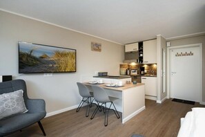Ett kompakt bostadsutrymme med ett litet kök, en matplats och ett stort fönster med utsikt.