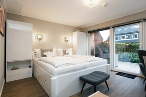A modern bedroom with a large bed, bedside tables, a wardrobe, and a sliding glass door leading to a balcony. - Holiday apartment with 1 bedroom (Westerland - Sylt)