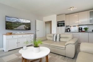 A modern living room with a sofa, a coffee table, and a television mounted on the wall. - Holiday apartment with 2 bedrooms (Westerland - Sylt)