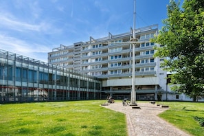 A multi-story building with a modern architectural design, featuring a glass facade and a central courtyard with a flagpole. - Holiday apartment with 2 bedrooms (Westerland - Sylt)