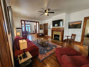 Ein geräumiges Wohnzimmer mit Kamin, roten Sofas, einem Couchtisch und einem Deckenventilator.