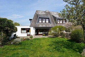 A two-story house with a sloped roof, a front porch, and a well-maintained lawn. - Holiday apartment in Sylt with swimming pool (Sylt)