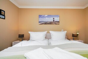 A hotel room with two beds, a painting of a lighthouse, bedside lamps, and a vase with flowers. - Holiday apartment in Sylt with swimming pool (Sylt)