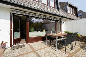 Un patio con mesa y sillas, una puerta corrediza de vidrio y un pequeño jardín con plantas.