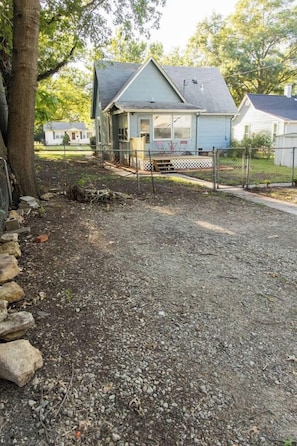 A residential property with a gravel driveway, a fenced yard, and a house with a gabled roof. - Cheerful & Homey ~ 7 Mins to Downtown ~ Queen Beds (Topeka)