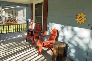 A porch with two Adirondack chairs and a small table, a welcome sign, and a view of a house in the background. - Cheerful & Homey ~ 7 Mins to Downtown ~ Queen Beds (Topeka)