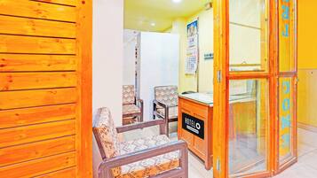 A hotel lobby with wooden paneling, a reception desk, two patterned chairs, and a glass door with 'WELCOME' signage.