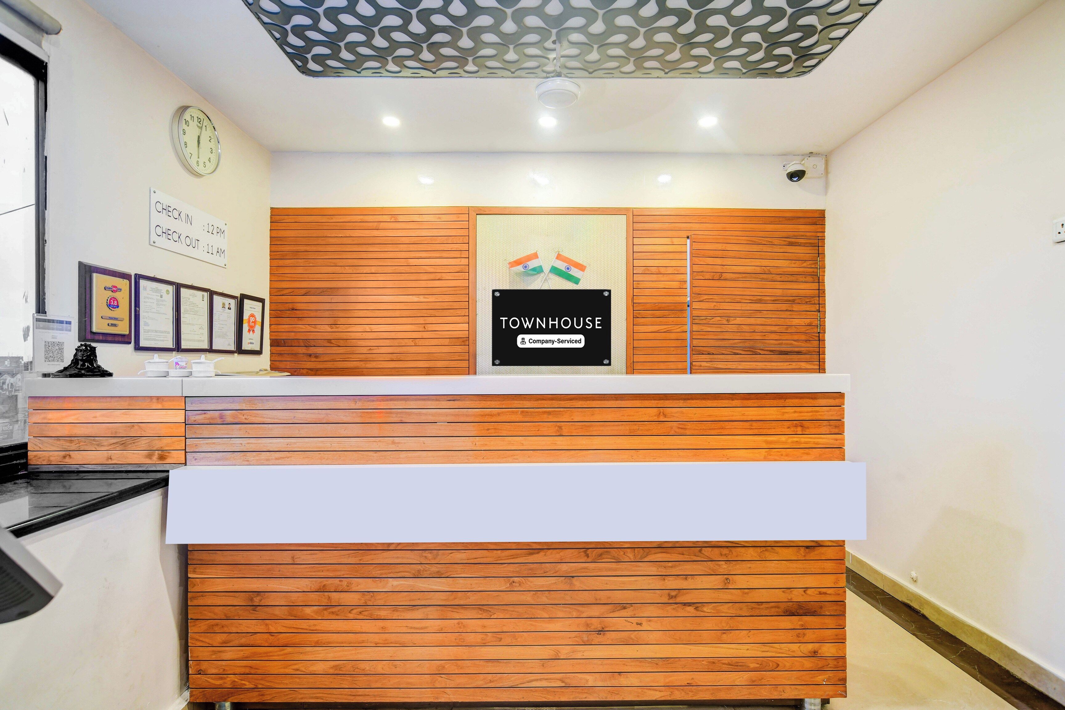 A reception desk with a wooden finish, a clock, and a sign indicating check-in and check-out times.