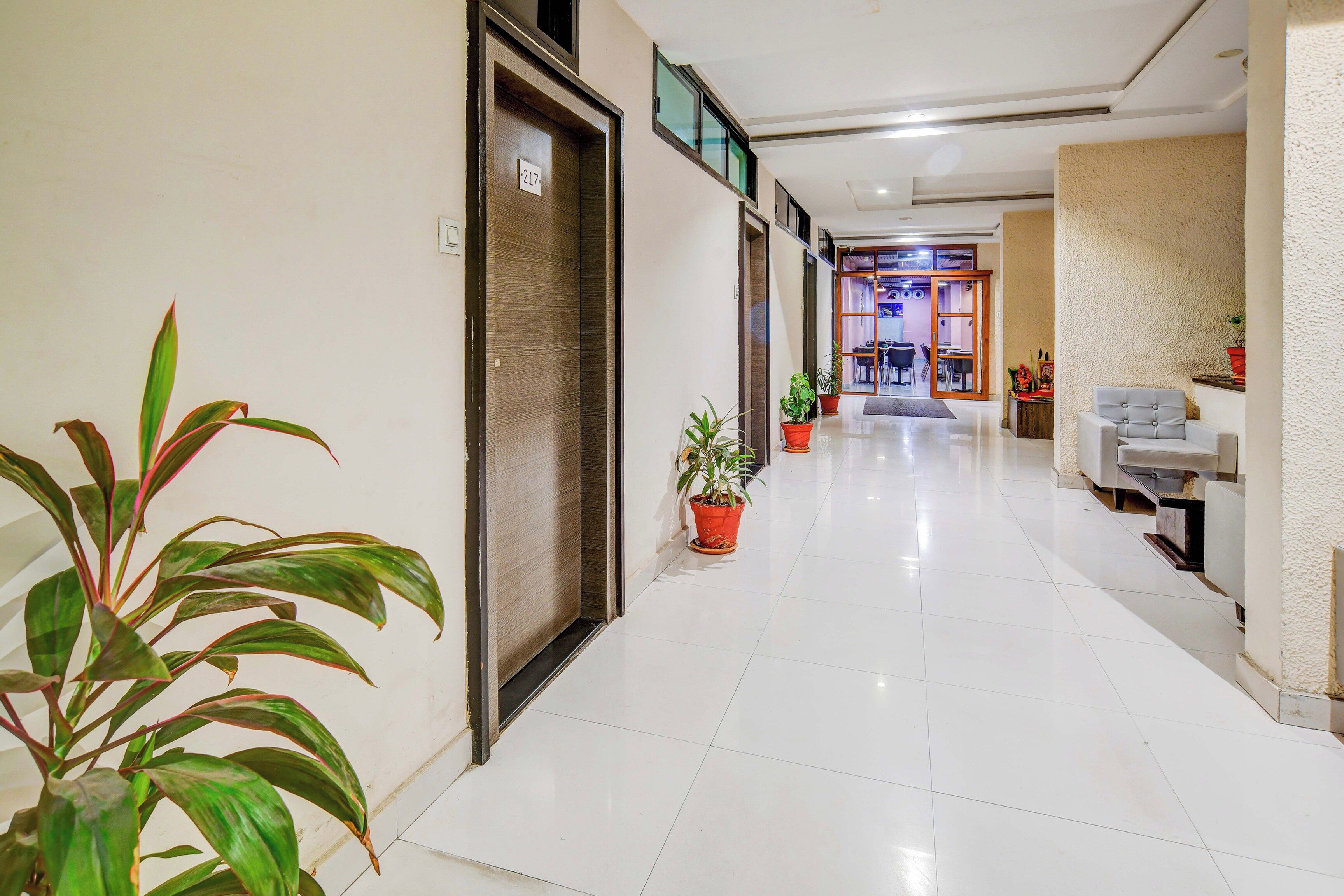 Un pasillo de hotel con piso de baldosas, plantas en macetas y una sala de estar con sofá y mesa.