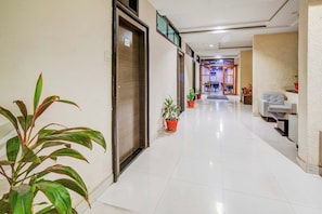 Un pasillo de hotel con piso de baldosas, plantas en macetas y una sala de estar con sofá y mesa.