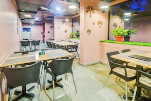 Een eethoek met tafels en stoelen, een wand met decoraties van bladeren, en een raam met planten.
