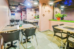 Comedor con mesas y sillas, una pared decorada con motivos de árboles y una ventana con plantas.