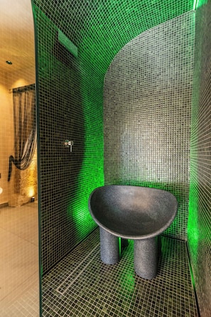 Un baño con una bañera independiente negra, iluminación verde y una zona de ducha con puerta de cristal.