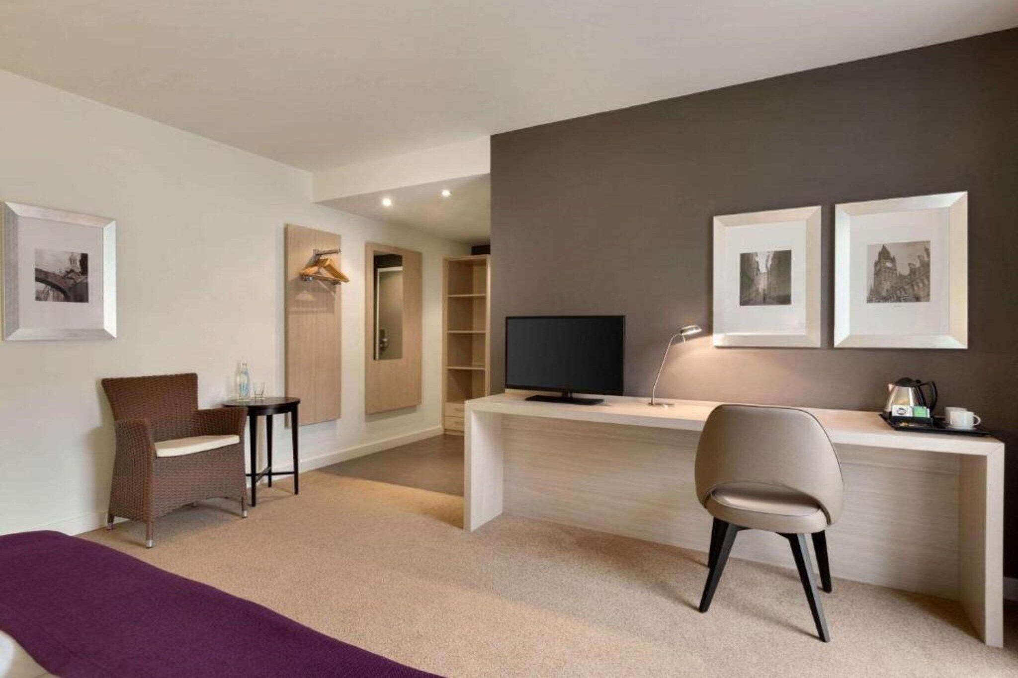 A modern hotel room with a desk, a chair, a television, and a bed.