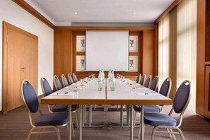 Un salón de conferencias con una larga mesa, sillas y una pantalla para proyector.