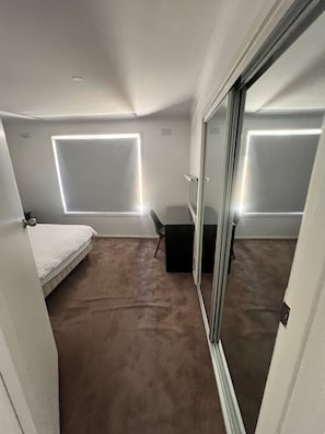 A small, carpeted room with a bed, a desk, and a sliding glass door. - Beautiful and spacious house in Doveton (Doveton)