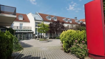 Ein Innenhof mit einem gepflasterten Weg, einem Gebäude mit geneigtem Dach und einer roten Struktur.