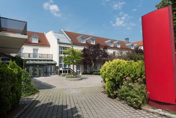 Ein Innenhof mit einem gepflasterten Weg, einem Gebäude mit geneigtem Dach und einer roten Struktur.