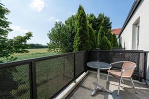 Ein Balkon mit einem Maschendrahtgeländer, einem runden Tisch und einem Korbstuhl.