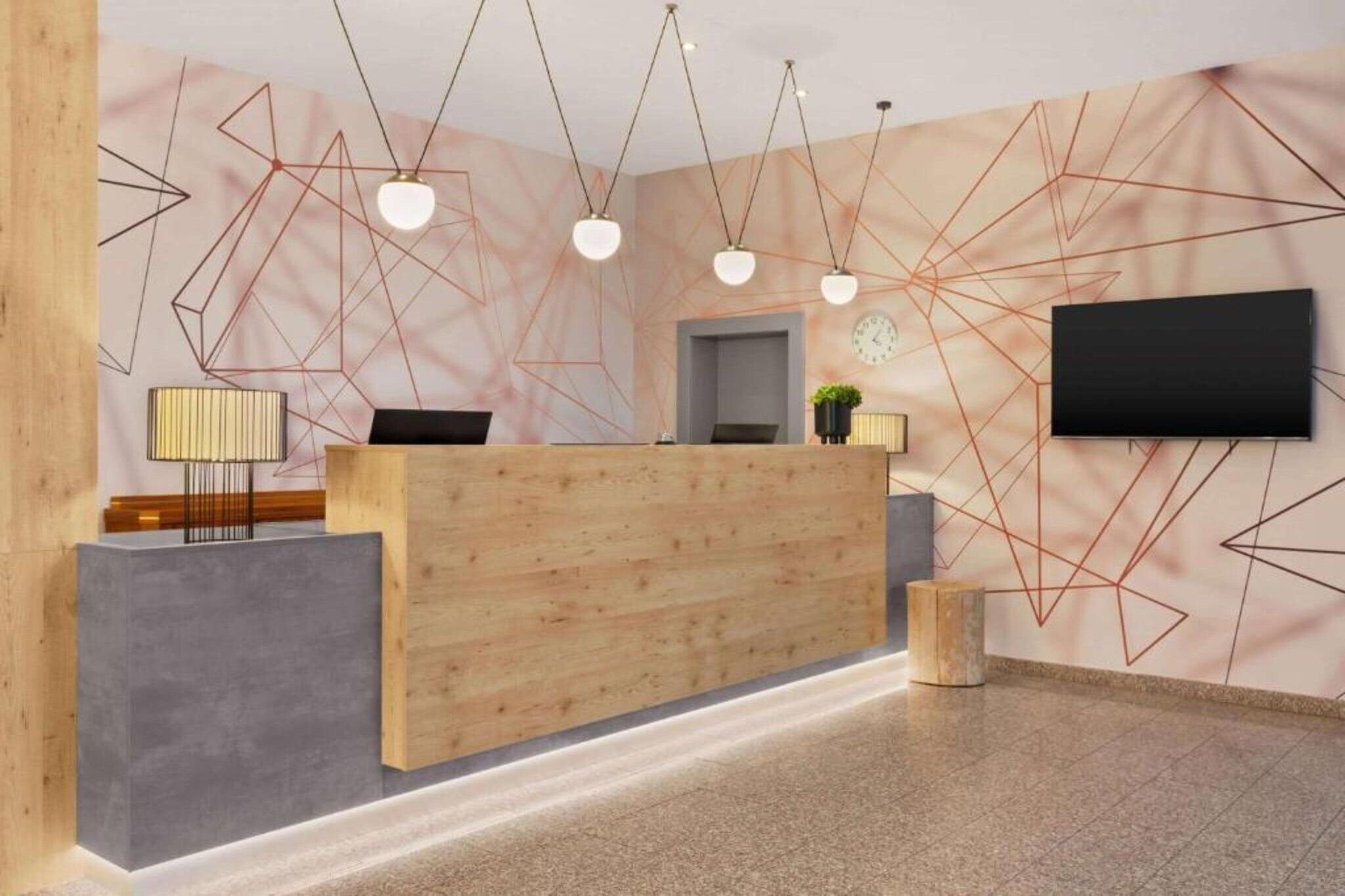 Ein Empfangstresen mit Holzoptik, ein flachbildschirm-Fernseher an der Wand und geometrische Wandbilder.