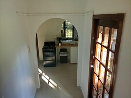 Un pasillo estrecho que conduce a una cocina con estufa, lavabo y ventana.