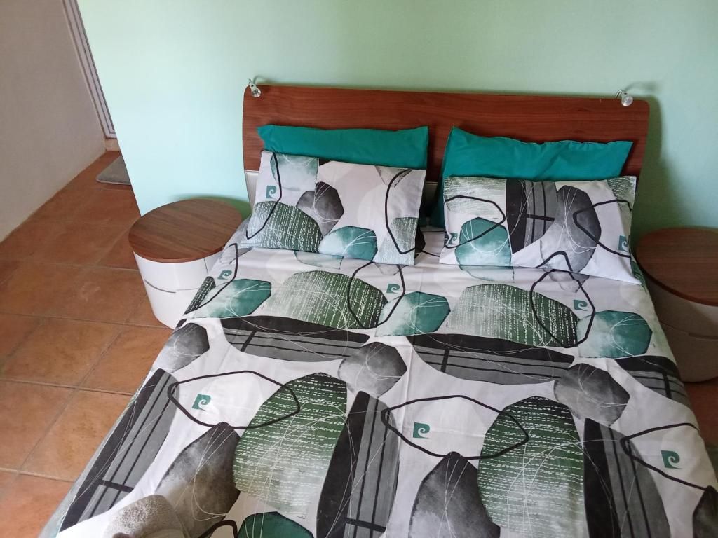 Cama com colcha estampada, cabeceira de madeira e duas almofadas com detalhes em azul-esverdeado.