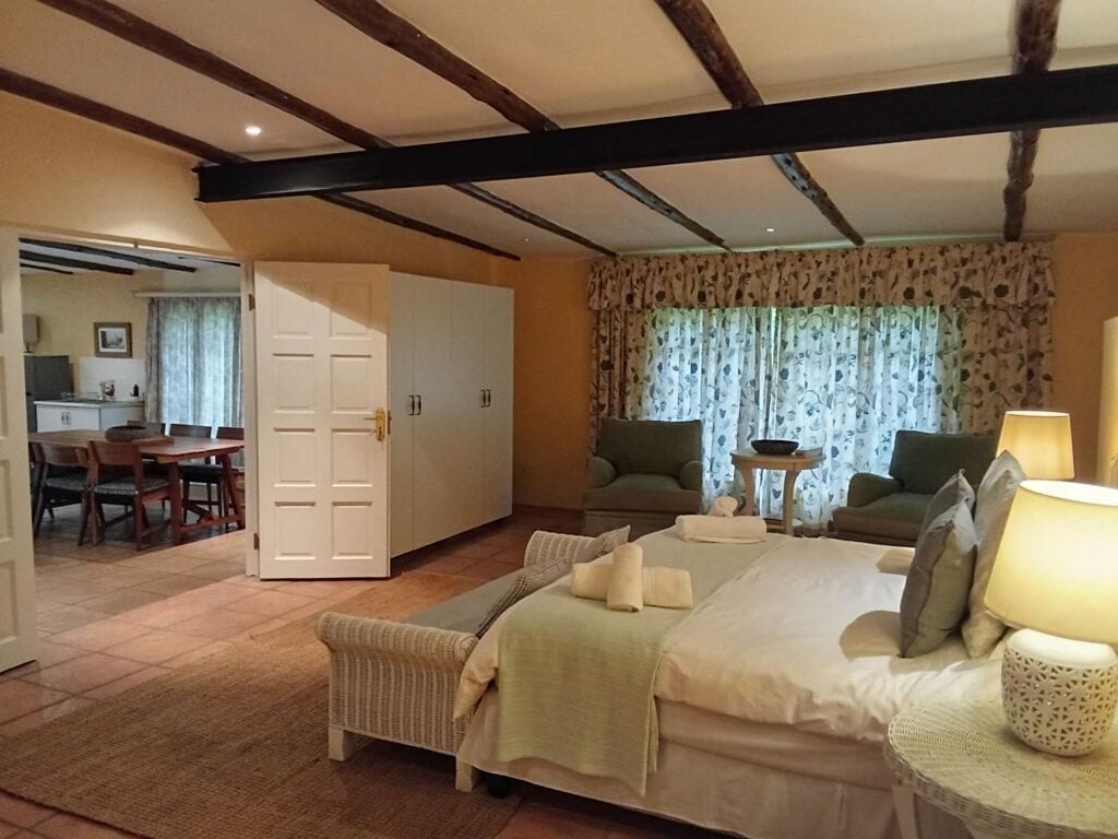 Een slaapkamer met een bed, een stoel, een tafel met een lamp en uitzicht op een eetgedeelte.