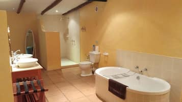 Een badkamer met een bad, twee wastafels, een toilet en een douchehoek.
