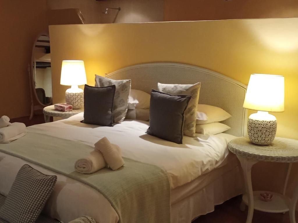 Et hotelværelse med en seng, to sengeborde med lamper, en sengegavl og et lille bord med lampe.