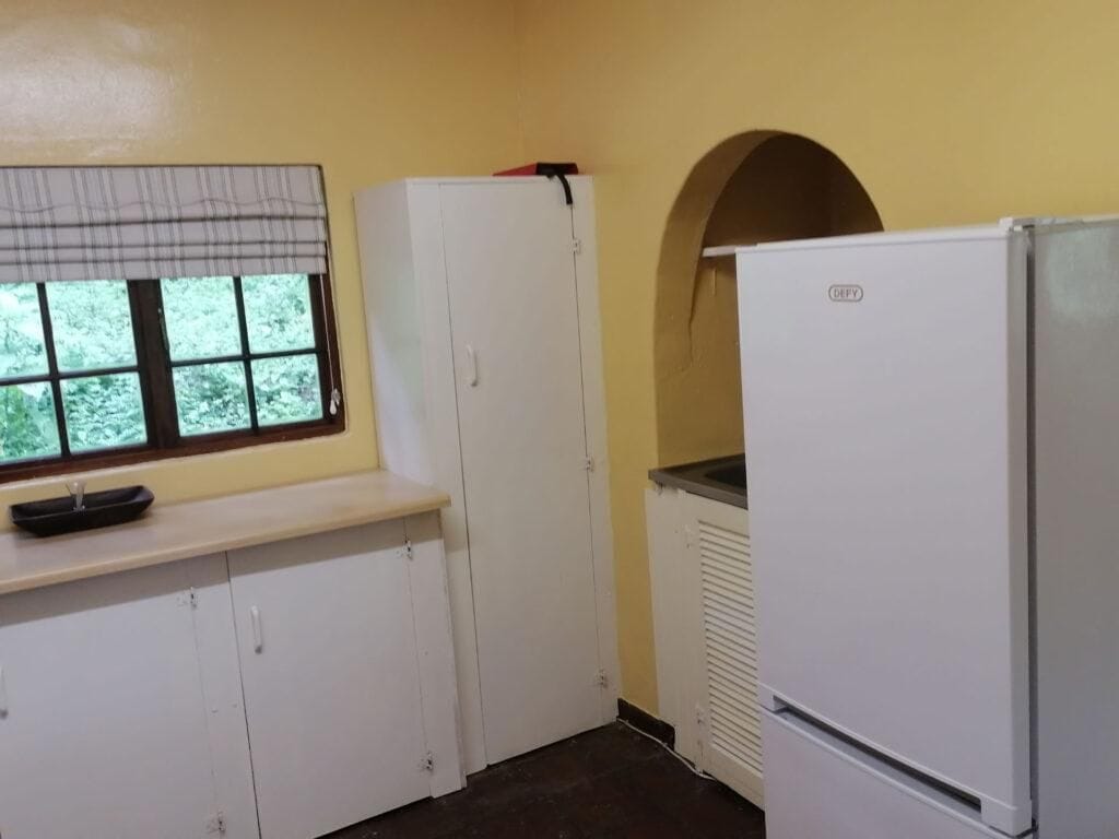 Une cuisine de taille réduite avec une fen être, des meubles blancs, un réfrigérateur blanc et un radiateur.
