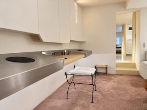 A modern kitchen with a built-in stove, a small stool, and a view into the adjacent bedroom. - Place Vendôme – A stylish and elegant apartment (Paris)